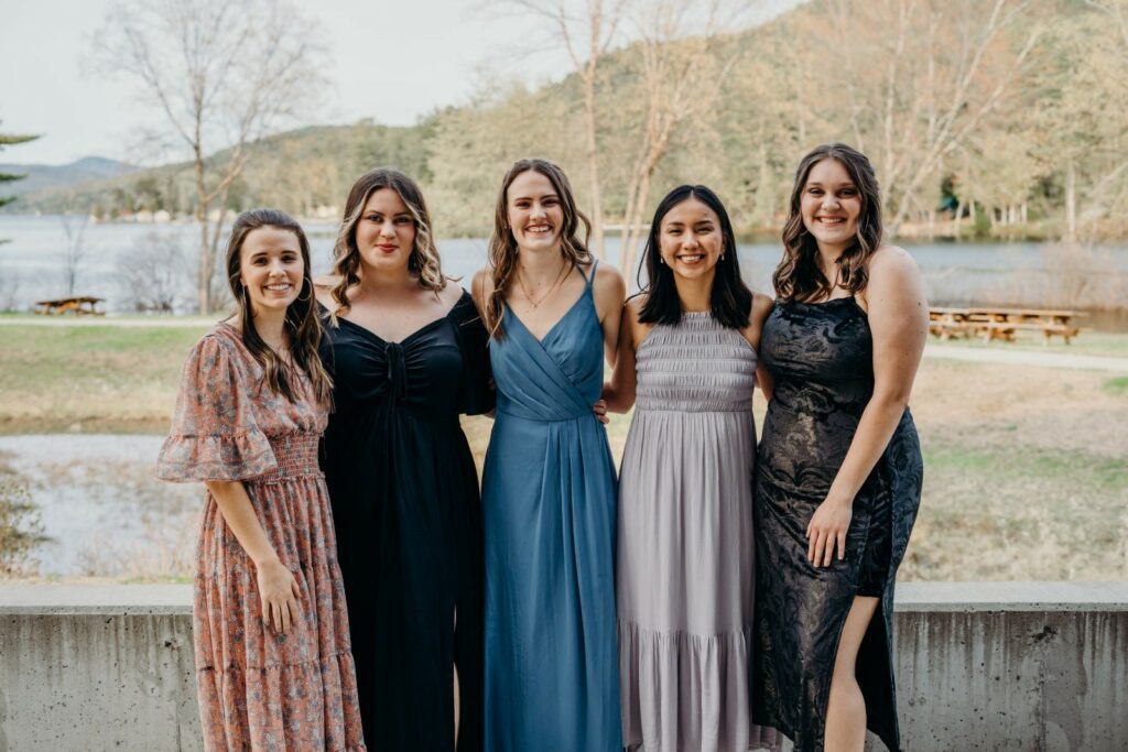 women smiling in dresses next to a lake